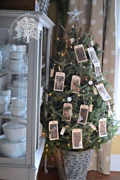 a small christmas tree with pictures on it in a basket next to a china cabinet