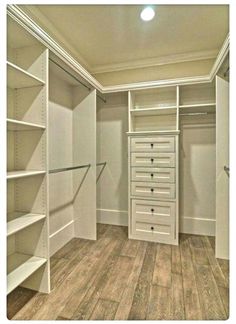 an empty walk in closet with shelves and drawers on the bottom shelf, next to a wooden floor