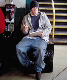 a young man sitting on top of a black box next to a phone and stairs