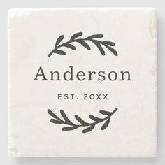 a square coaster with the name and image of an olive branch in black ink on white marble