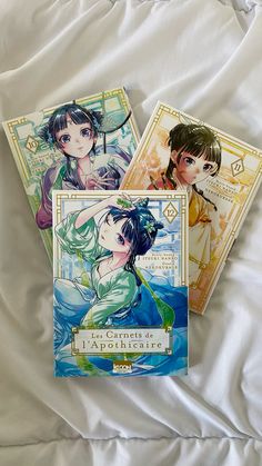 three anime book covers laying on top of a bed next to each other, one with an image of two women