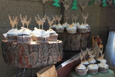 cupcakes with white frosting and deer heads on them are sitting on a tree stump