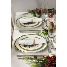 the table is set for christmas dinner with green and white plates, silverware, napkins and greenery