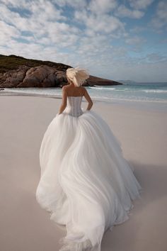 a woman in a wedding dress walking on the beach with her back to the camera