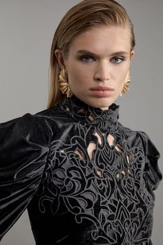 a woman in a black dress with gold earrings on her head and shoulders, looking at the camera