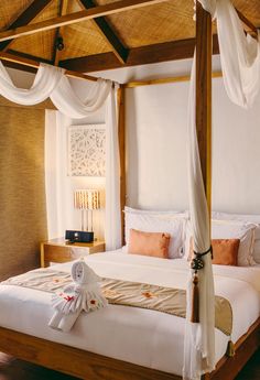 a bed with white drapes and pillows on it's sides, in a bedroom