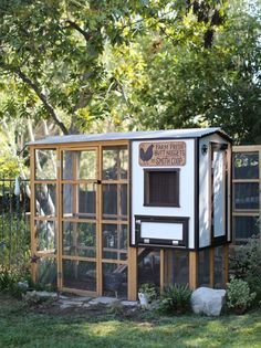 a small chicken coop in the middle of a yard with trees and bushes around it