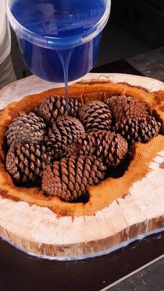 pine cones are being poured into a bowl on top of a wood slab with blue paint