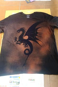 a t - shirt with a dragon on it sitting on the floor next to a piece of paper