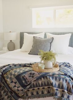 a bed with pillows, blankets and a basket on it in a room that has white walls