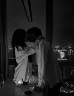 a man and woman kissing in front of a window with the city lights behind them