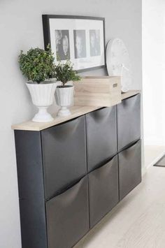 a white vase sitting on top of a black cabinet next to a potted plant