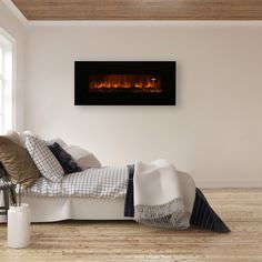 a bed with pillows and blankets on it in front of a wall mounted fire place