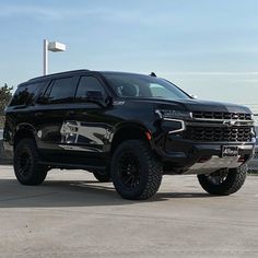 a large black truck parked on top of a parking lot next to a flag pole