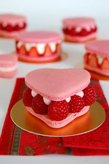 there is a heart shaped cake with raspberries on it and other desserts in the background