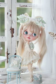 a doll with long blonde hair standing next to a chair and window in a white room