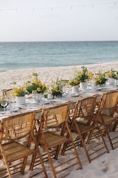 a long table set up on the beach for an outdoor dinner with flowers in vases