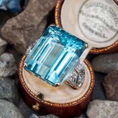 This stunning circa 1940s yellow gold cocktail ring is centered with an emerald cut aquamarine, weighing 33.06 carats, in a four-prong setting. The platinum topped shoulders are accented with milgrain and engraving details and is bead set with three (3) round single cut diamonds. The ring measures 21.8mm at the top, rises 12.1mm above the finger, tapering to 1.7mm wide and 0.7mm thick at the base of the shank. This ring is currently a size 8. The stone has very light abrasions but nothing that distracts from its beauty. Huge Diamond Rings, Aquamarine Cocktail Ring, Gem Rings, Blessed Wednesday, Yellow Gold Cocktail Ring, Alexis Bittar Jewelry, Princess Jewelry, Woman Jewelry, Gold Cocktail Ring