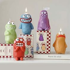 three candles with different colored monsters on top of each one and two boxes behind them