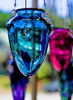 two colorful glass vases hanging from a wooden pole with strings attached to them, one is blue and the other is pink