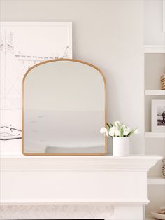 a mirror sitting on top of a white mantle next to a vase filled with flowers