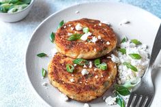 two crab cakes are on a plate with rice and green onions next to a fork