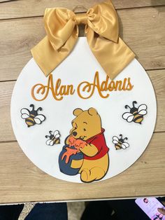 a winnie the pooh sign hanging on a wall with a ribbon around it's neck