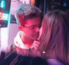 a man and woman kissing in front of a neon sign