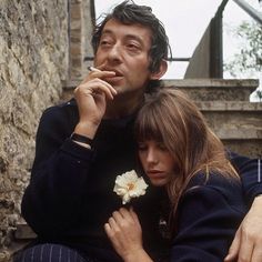 a man and woman sitting next to each other in front of a stone wall with stairs