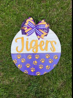 a purple and yellow sign that says tigers with paw prints on the front in grass