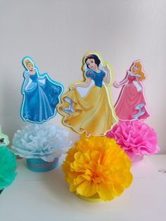 there are some paper decorations that look like disney princesses on the table with tissue pom poms