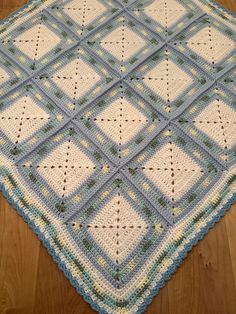 a blue and white crocheted blanket sitting on top of a wooden floor next to a rug