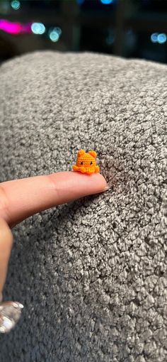 a tiny orange animal sitting on top of a gray couch next to a person's finger