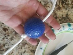 a hand holding a blue ball on top of a white plate next to a knife