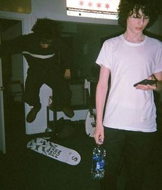 a young man holding a water bottle standing in front of a skateboard and tv