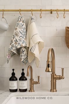 a kitchen sink with towels hanging on the wall and soap bottles in front of it