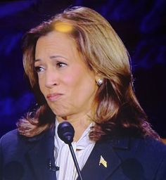 a woman standing at a podium with a microphone in front of her and looking off to the side