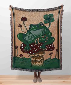 a woman standing in front of a tapestry with a frog sitting on top of a mushroom