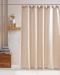 a white shower curtain in a bathroom next to a wooden shelf with towels on it