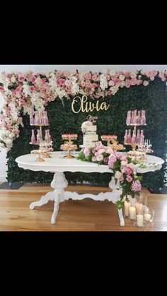 a table topped with cake and candles next to a flower covered wall filled with greenery