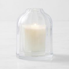 a clear glass candle holder with a lit candle in the middle on a white surface