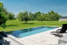 an empty chair sitting next to a pool in the middle of a lush green field