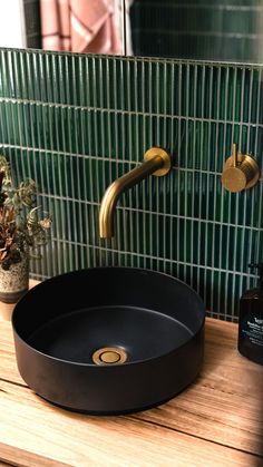 a black sink sitting on top of a wooden counter next to a green tiled wall