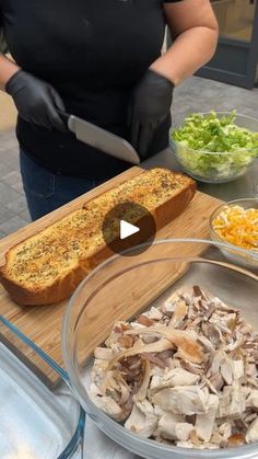 a woman in black shirt preparing food on wooden cutting board next to glass bowl filled with salad