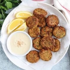 a white plate topped with meat patties next to a bowl of ranch dressing and lemon wedges