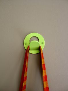 an orange and yellow scarf hanging on the wall next to a green circle shaped hook