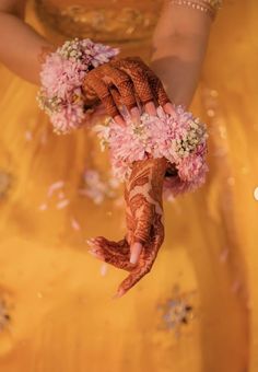 a woman in a yellow dress holding flowers and her hands with henna on it