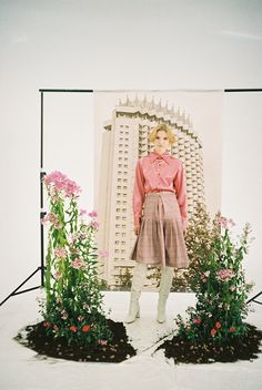 a mannequin dressed in pink stands next to some flowers and plants on a white background