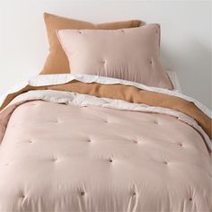 a bed with pink comforter and two pillows on top of it, in front of a white wall