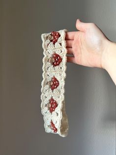 a hand holding up a crocheted piece of cloth with red flowers on it